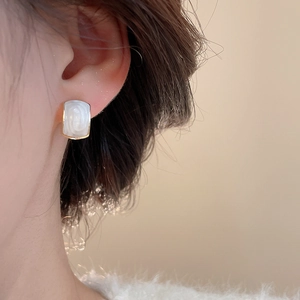 Close-up of elegant square pearl stud earrings with gold trim worn on a female ear