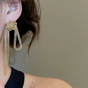 Close-up detail of golden braided knot earrings with long metallic fringe tassels
