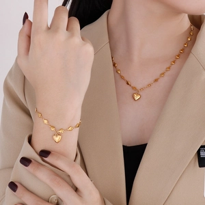 Elegant gold heart pendant necklace and bracelet set for women worn with beige blazer