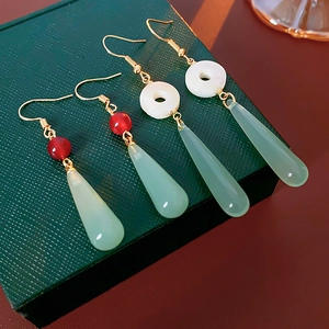 Detail of two pairs of resin drop earrings with gold hooks on a green textured box