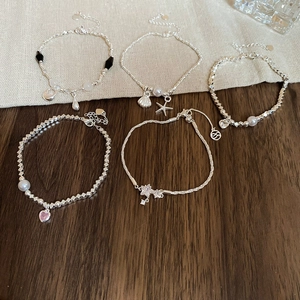 Dettaglio di braccialetti in argento con cuori rosa, perle e ciondoli a stella