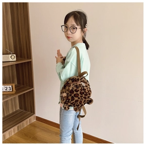 Detail view of a leopard print plush toddler backpack worn by a child in a home setting