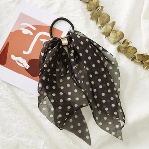 Close-up of black polka dot bow hair tie with a gold buckle on white fabric