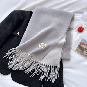 Detail of light gray knit scarf with fringes and logo label on black blazer