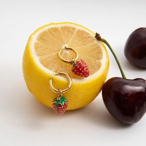 Detail of 18K gold stainless steel hoop earrings with red enamel strawberry charms on lemon