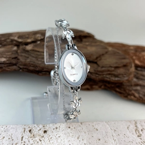 Detail of silver oval quartz watch with leaf-shaped rhinestones on acrylic stand