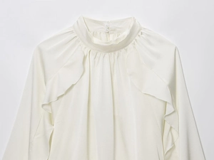 Close-up of white ruffled long sleeve blouse with stand collar and creped fabric texture