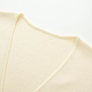 Close-up of V-neckline on a cream knit vest showing premium stitching and fine texture