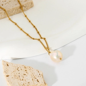 Detailed view of the large white baroque pearl pendant on a gold beaded chain necklace