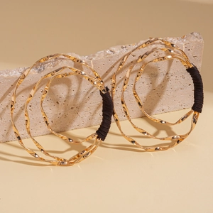 Twisted gold metal bracelets with black fabric wrap on natural stone aesthetic background