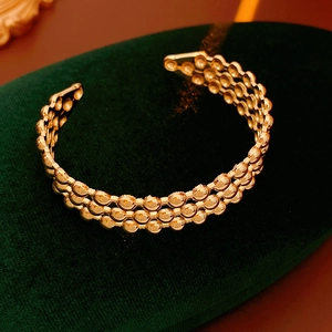 Macro di un bracciale a tre file di perle dorate su un espositore di velluto verde scuro