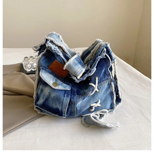 Detail of blue washed denim bag featuring frayed edges and white lace-up side design