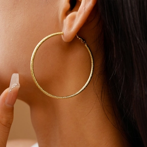 Close-up of a large gold hoop earring with a textured matte finish worn by a model