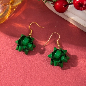 Detailed macro view of forest green ribbon bow earrings with gold hooks on red background