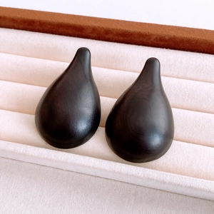 Macro shot of dark wooden teardrop resin earrings on a beige velvet jewelry tray