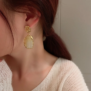 Close-up of a woman wearing vintage geometric earrings with creamy resin and gold frames