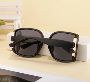Detail of black sunglasses with dark gray lenses and premium gold metal hinge accents
