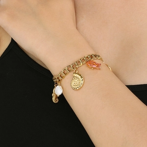Gros plan d'un bracelet océan doré avec breloques coquillage, nautile et poisson