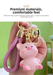 Pink cartoon pig keychain with purple braided leather strap and gold metal bell