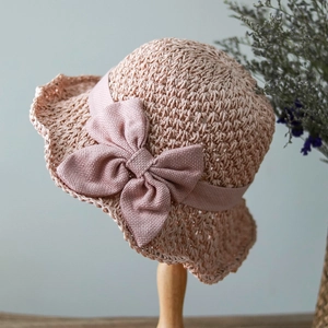 Detailed close-up of pink straw sun hat with woven bow accent on a wooden display