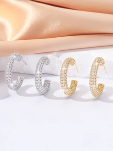 Close-up of C-shaped pave hoop earrings in gold and silver finish with white zircons