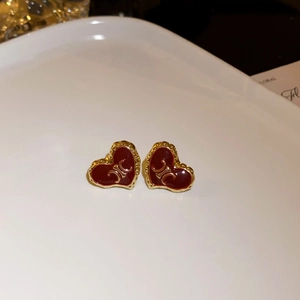 Detail showing red enamel heart stud earrings with golden trim and luxury pattern
