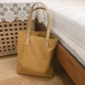 Close-up of yellow canvas tote bag featuring leather handles and metal rivets