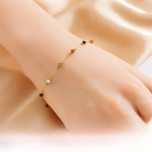 Close-up of a gold stainless steel chain bracelet with colorful stone beads on silk background