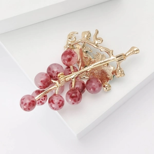 Gros plan d'une broche raisin en émail doré avec perles roses sur support blanc