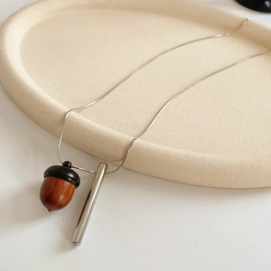 Detail of wooden acorn pendant and silver metal bar on a sleek snake chain necklace