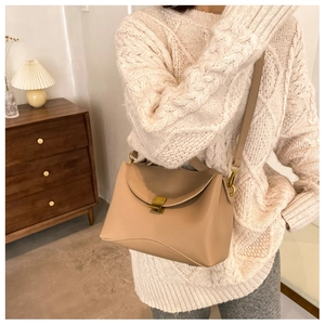 Detail of khaki leather crossbody bag with gold buckle on model in cozy beige knitwear