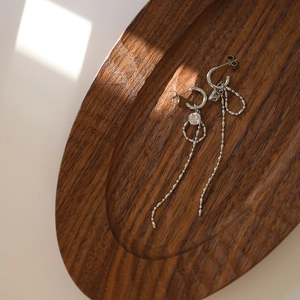 Detail shot of silver tassel bow earrings with sparkling cubic zirconia on a wood tray