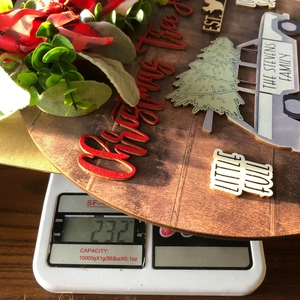 Weight display of round wooden Christmas door sign with 3D red text on a digital scale