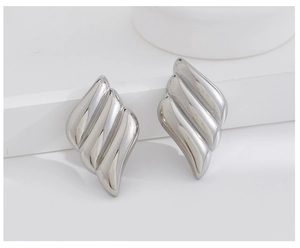 Macro shot of silver-plated wing stud earring with wavy texture on white tiered stand