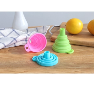 Drei bunte, faltbare Silikontrichter in Pink, Grün und Blau auf einem Holztisch
