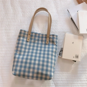 Detailed view of blue gingham canvas tote bag with beige leather straps and gold rivets