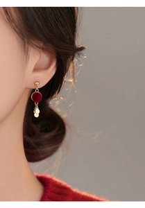 Close-up of model wearing red flocked round fringe earrings with gold metal accents