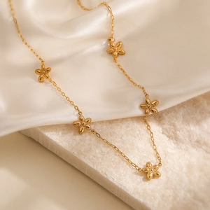 Minimalist gold necklace with five small floral pendants on a white stone background