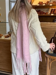 Close-up of a pink knitted scarf with decorative tassels worn in a cozy cafe setting