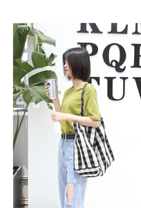 Detail of checkered canvas tote bag held by model wearing a green t-shirt and jeans