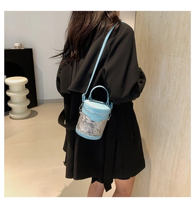 Detail of light blue bucket bag with white floral pattern on a woman's shoulder