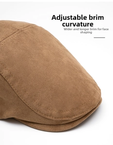 Detail of a brown suede newsboy cap featuring wide curved brim and reinforced stitching