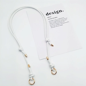 Detail of adjustable white leather bag strap with gold spring clips and knot accents