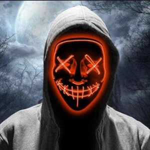 Macro view of orange LED glowing mask with cross eyes design in a spooky forest setting
