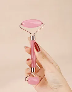 Close-up of rose quartz facial roller with rose gold metal frame held by hand