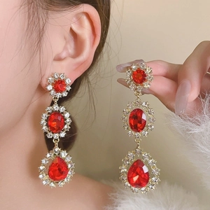 Close-up of luxury red gemstone earrings with gold tassels and sparkling rhinestones