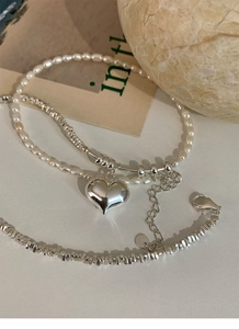 Detail of silver beaded necklace and pearl bracelet with heart charm on aesthetic background