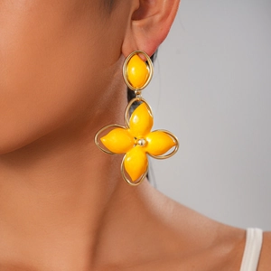 Close-up of a model wearing yellow enamel flower drop earrings with golden metal frames