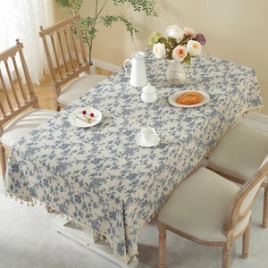 Close-up of beige cotton linen tablecloth with blue floral prints and tassel fringe