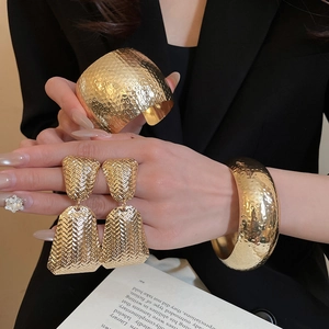 Close-up of hammered gold bangle and woven earrings worn by a model in a black suit